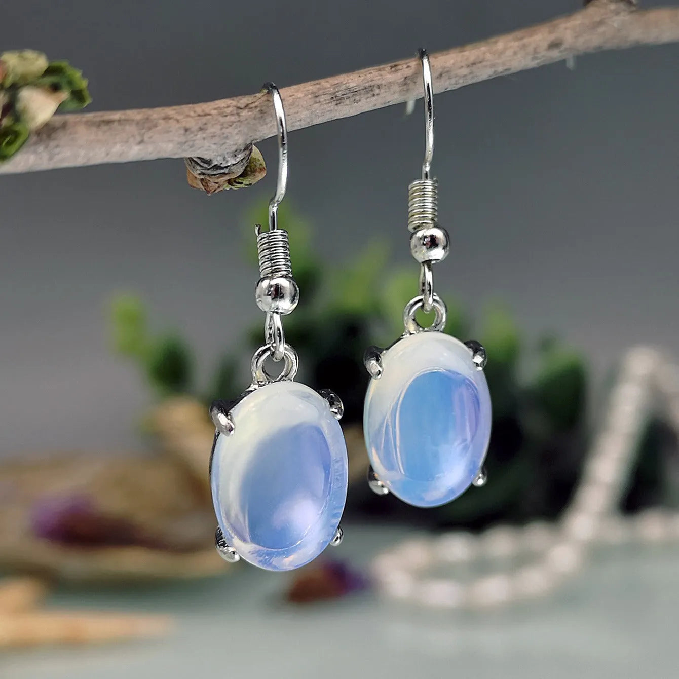 Pair of pale opal-colour drop earrings with a small cross detail on an elliptical alloy pendant.
