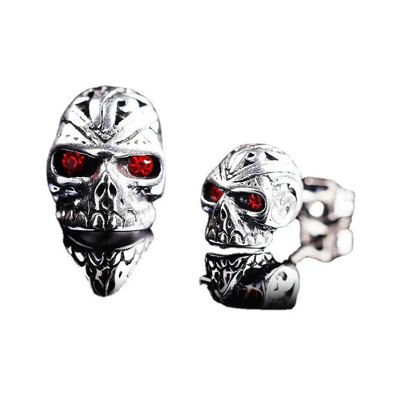 Pair of red eye skull stud earrings with alloy and gemstone inlay on a white background.