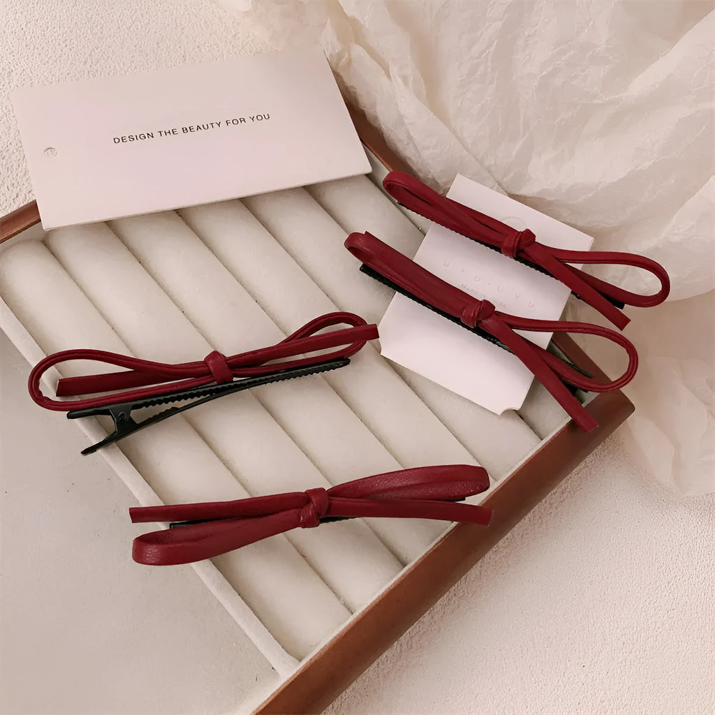 Close-up of a wine red leather bow-shaped barrette hair clip on a dark background.
