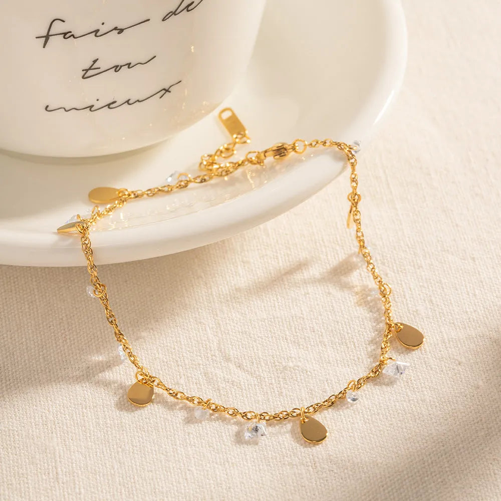 Close-up of a women's stainless steel anklet with a geometric water drop tassel charm on an adjustable chain.