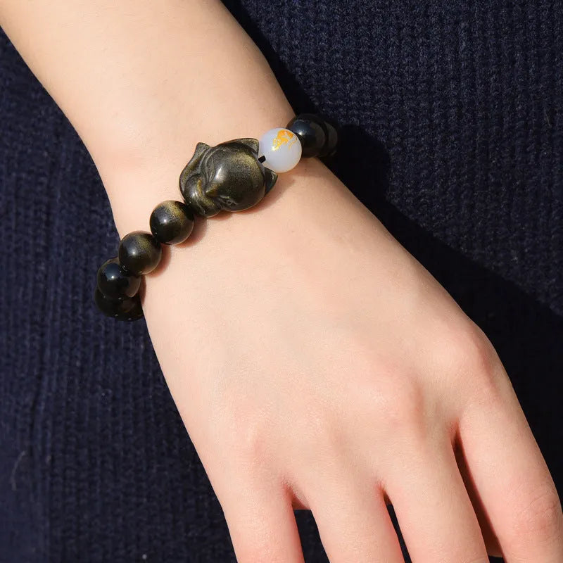 Natural black obsidian bracelet with 10mm beads on wrist, showing gold tone fastening option.