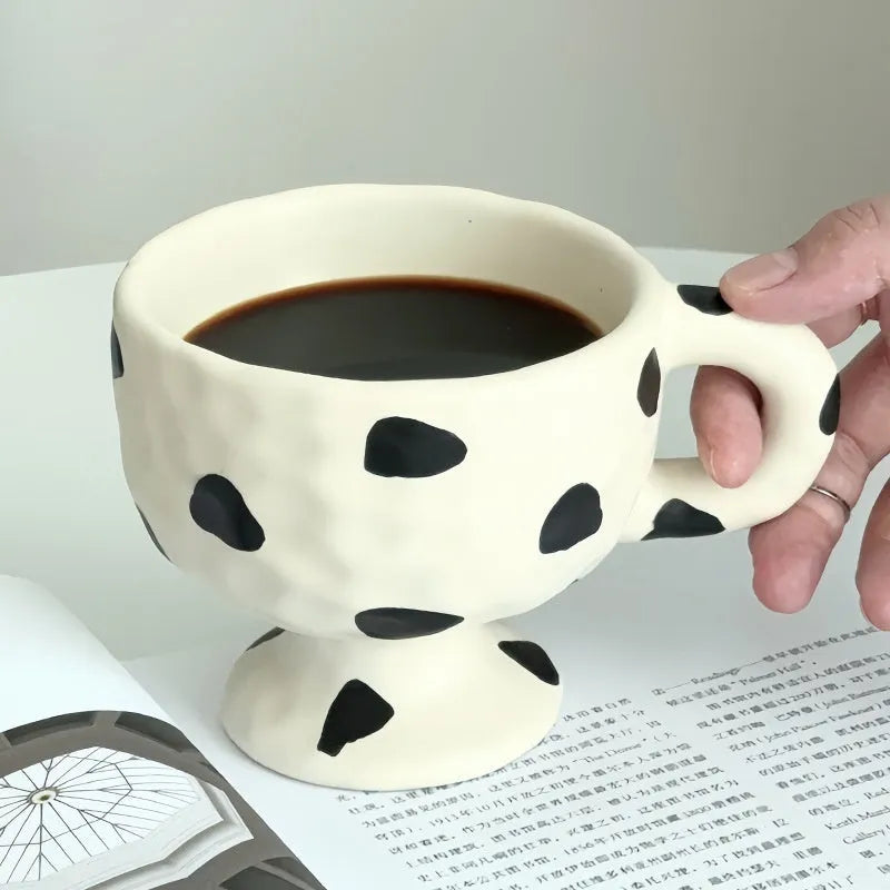 Hand-pinched irregular shaped ceramic mug in a solid colour, shown on a table.