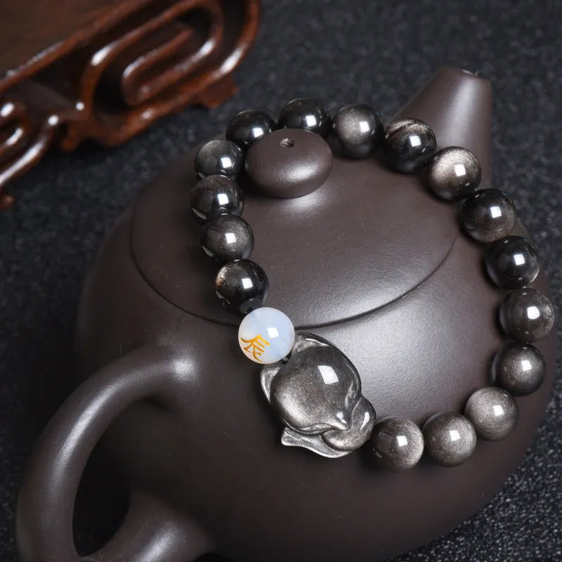Natural black obsidian bracelet with 10mm beads on wrist, showing gold tone fastening option.