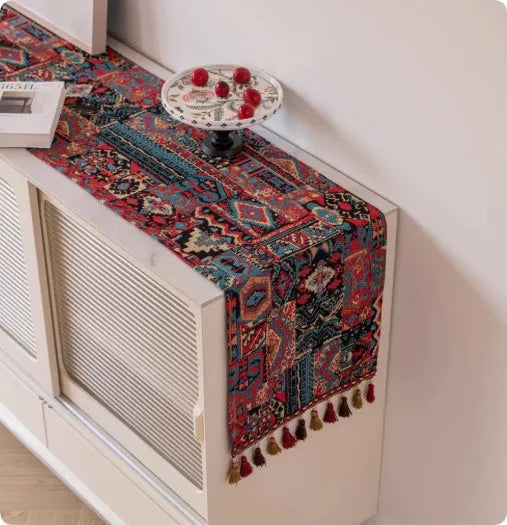 Long European-style retro table runner with decorative tassels in a floral design on a wooden table.