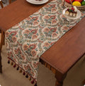 Long European-style retro table runner with decorative tassels in a floral design on a wooden table.