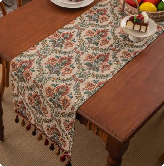 Long European-style retro table runner with decorative tassels in a floral design on a wooden table.