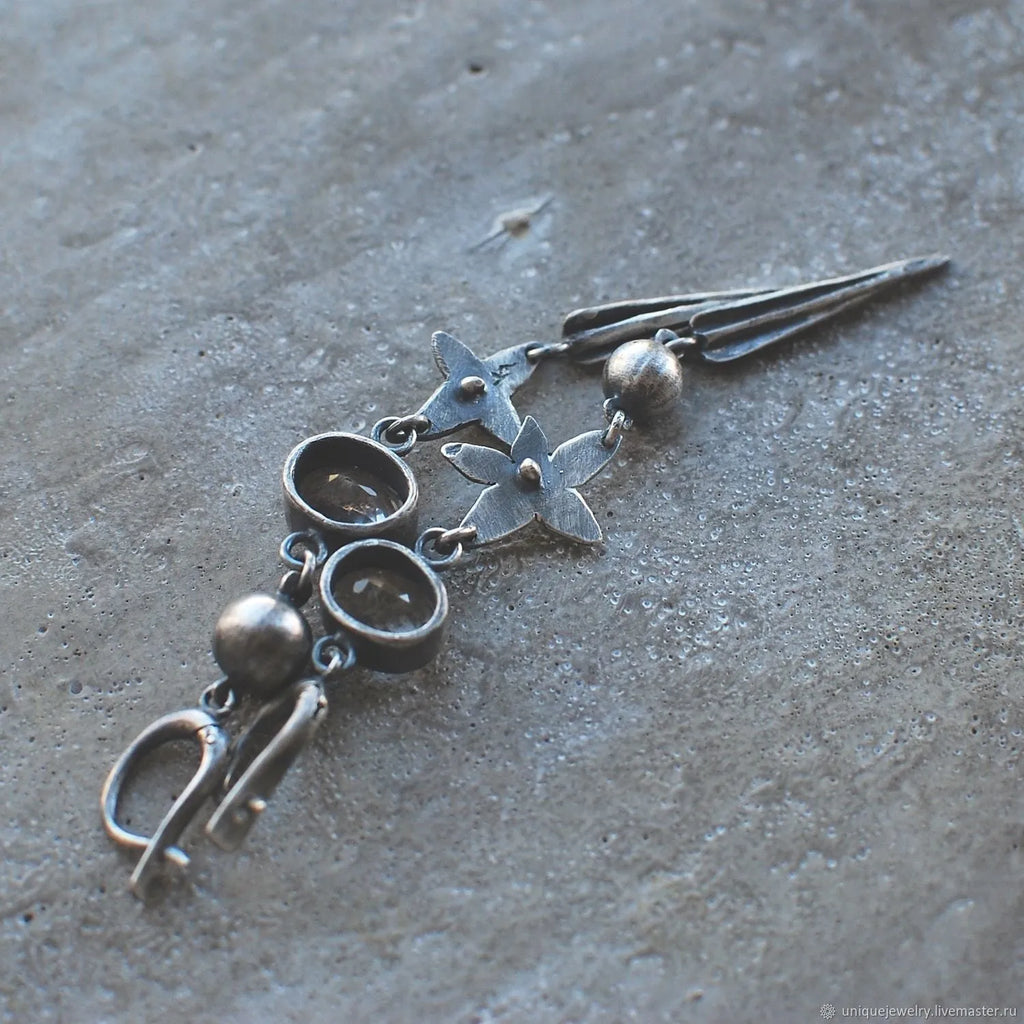 Pair of long geometric pendant earrings in antique silver with rhinestone detail on a white background.
