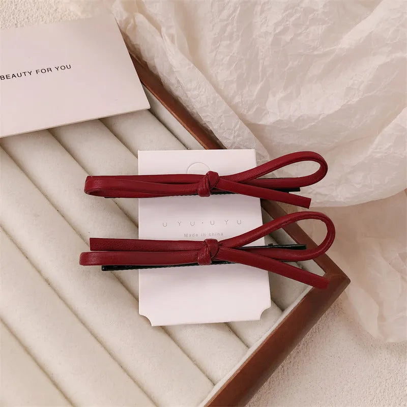 Close-up of a wine red leather bow-shaped barrette hair clip on a dark background.