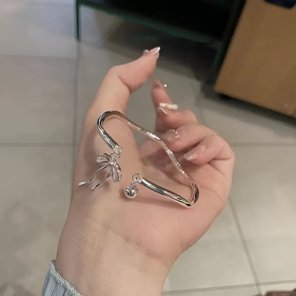 Silver adjustable bracelet with a detailed bow charm and bell opening.
