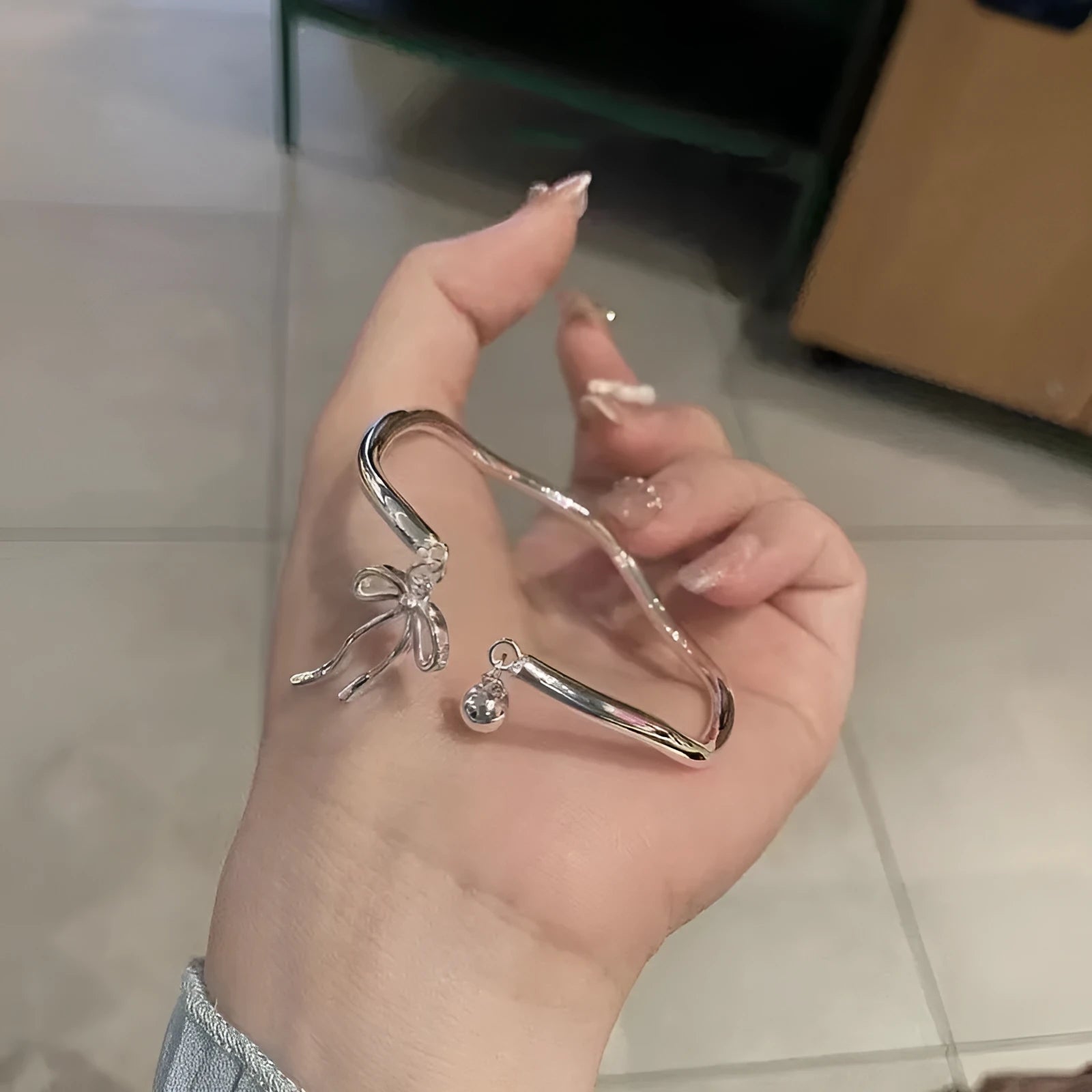 Silver adjustable bracelet with a detailed bow charm and bell opening.