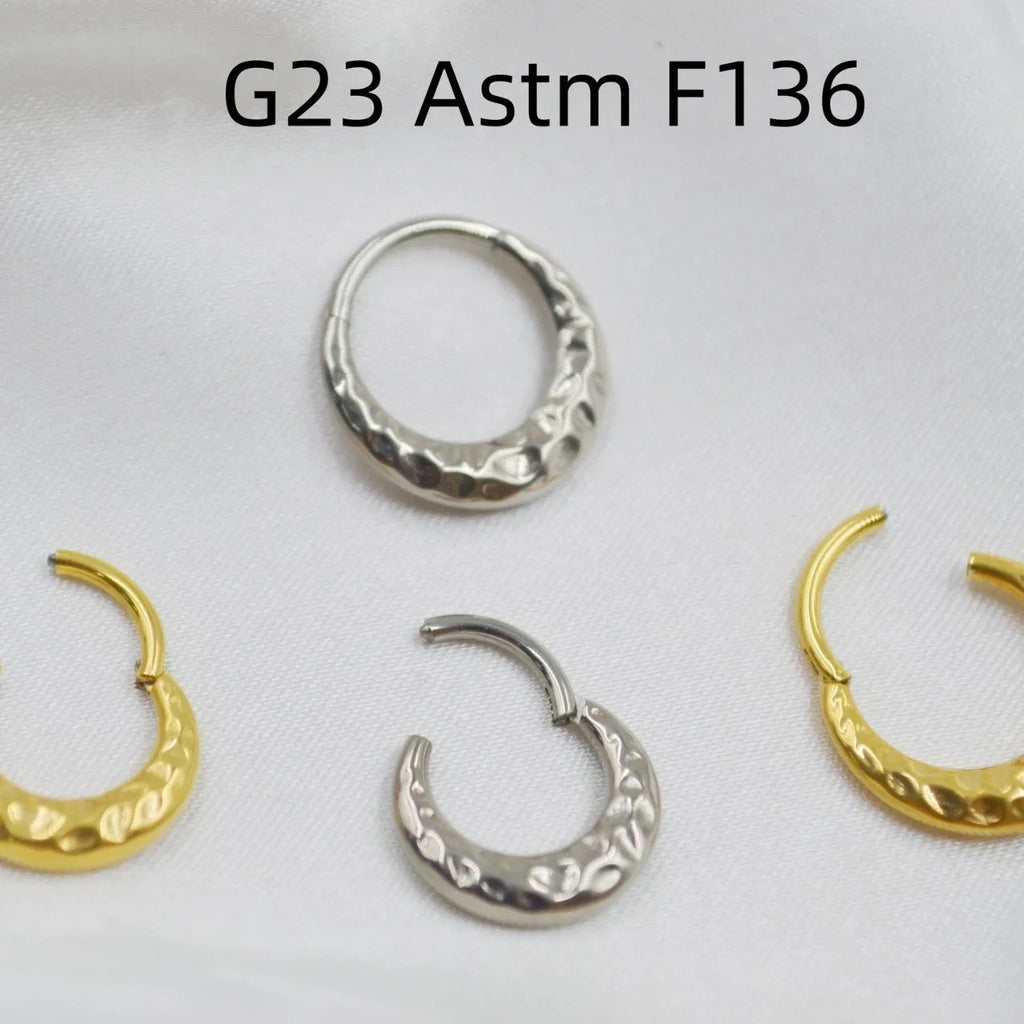 Close-up of a carved concave-convex titanium nose ring in gold finish, showing textured surface.