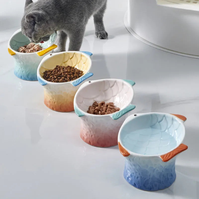 Blue fish-shaped ceramic cat bowl with tilted design on a wooden surface.