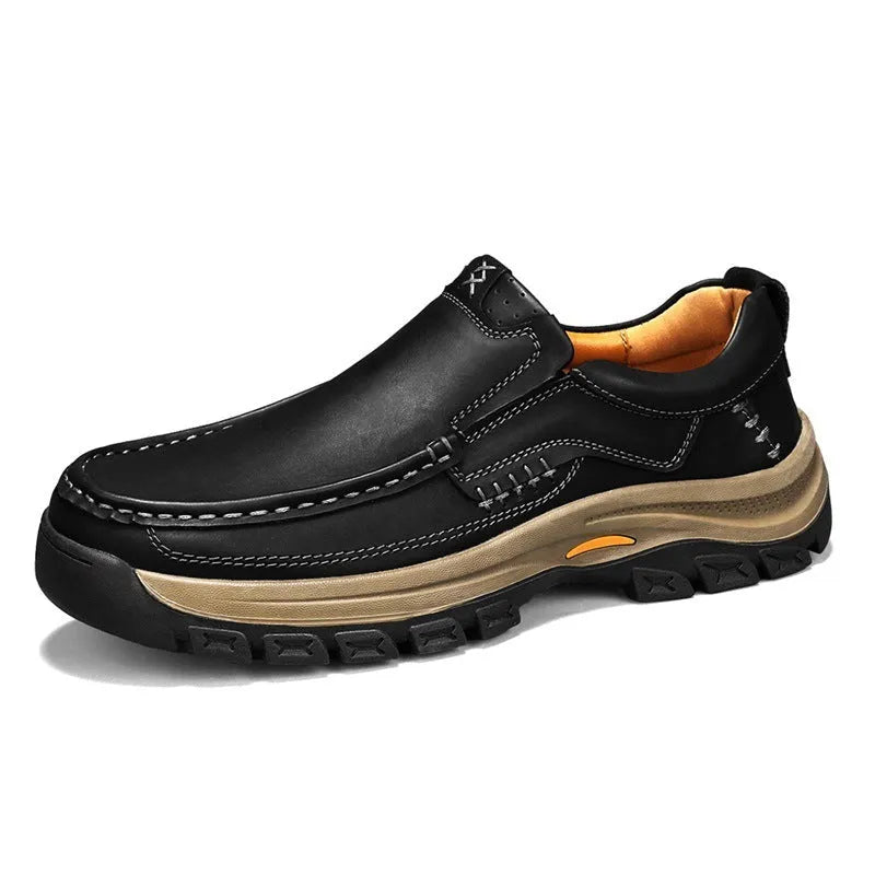 Men's black leather mountaineering shoes with thick rubber soles and round toe on a rocky path.