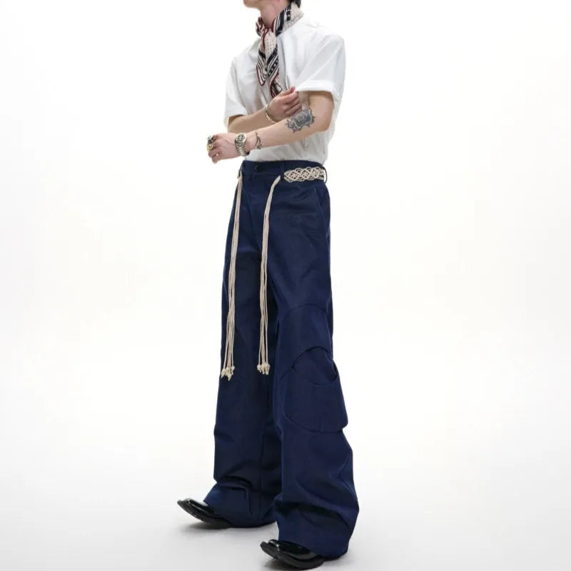 Men's dark blue straight-leg jeans showing heavy belt stitching, 3D cutting, zipper decoration, and a loose fit.