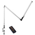 Black LED clip desk lamp with adjustable folding arm and remote control on a wooden desk.
