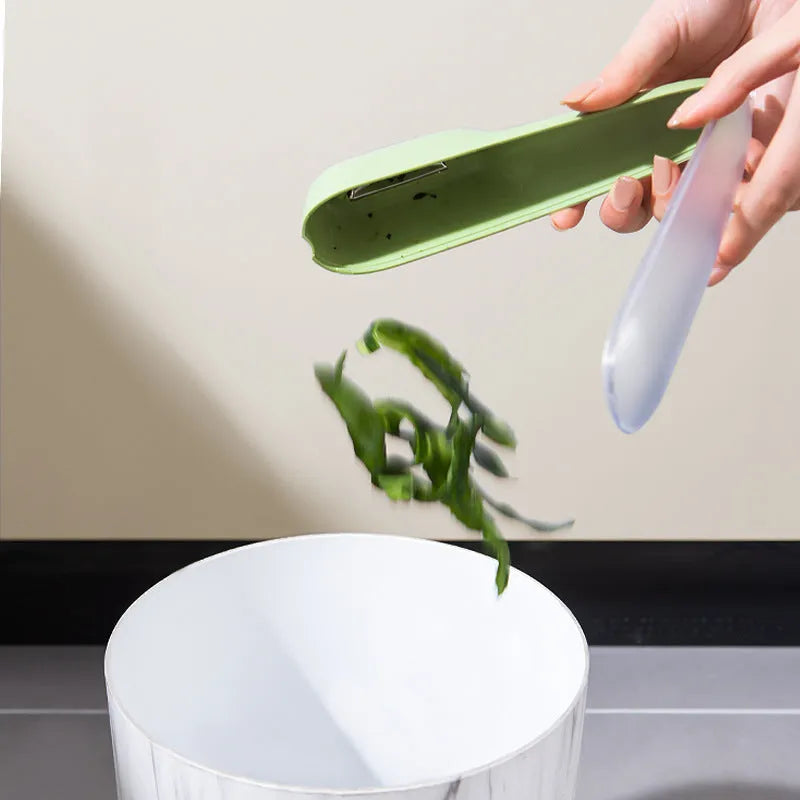Green vegetable and fruit peeler with a storage tube and stainless steel blade on a kitchen counter.