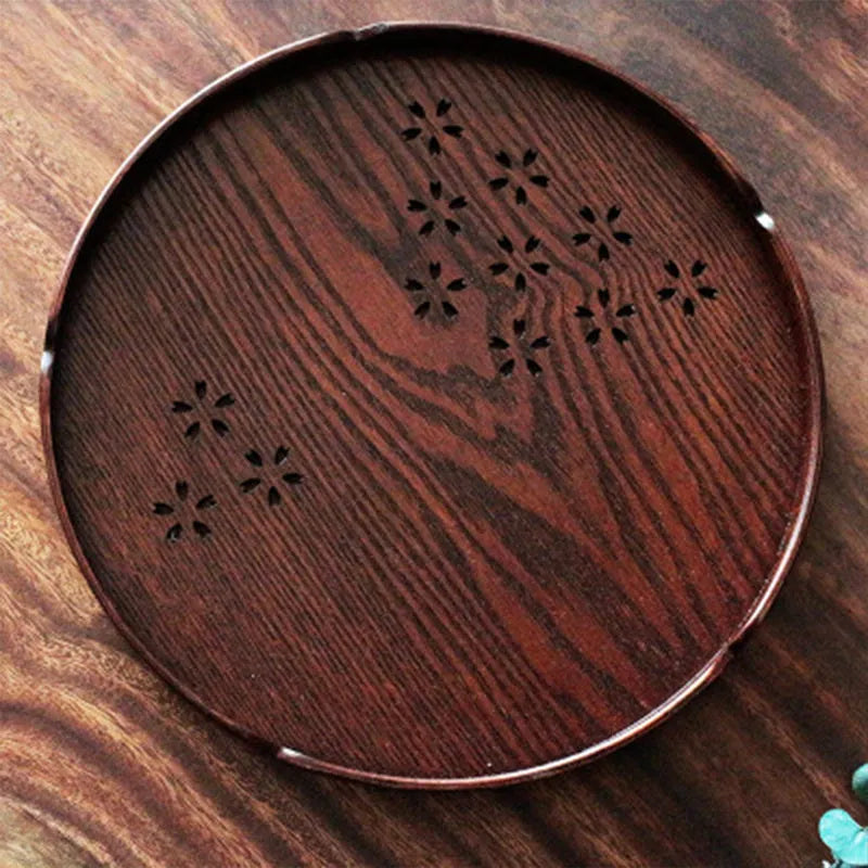 Twelve wooden dessert plates with carved cherry blossom design arranged in storage tray