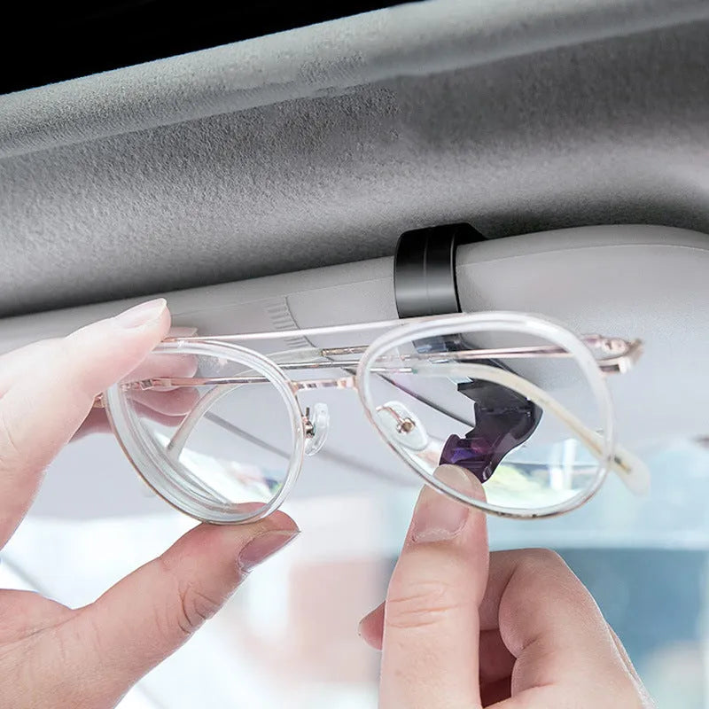 Black plastic multifunctional car mounted glasses and card clip attached to a sun visor holding sunglasses and an ID card