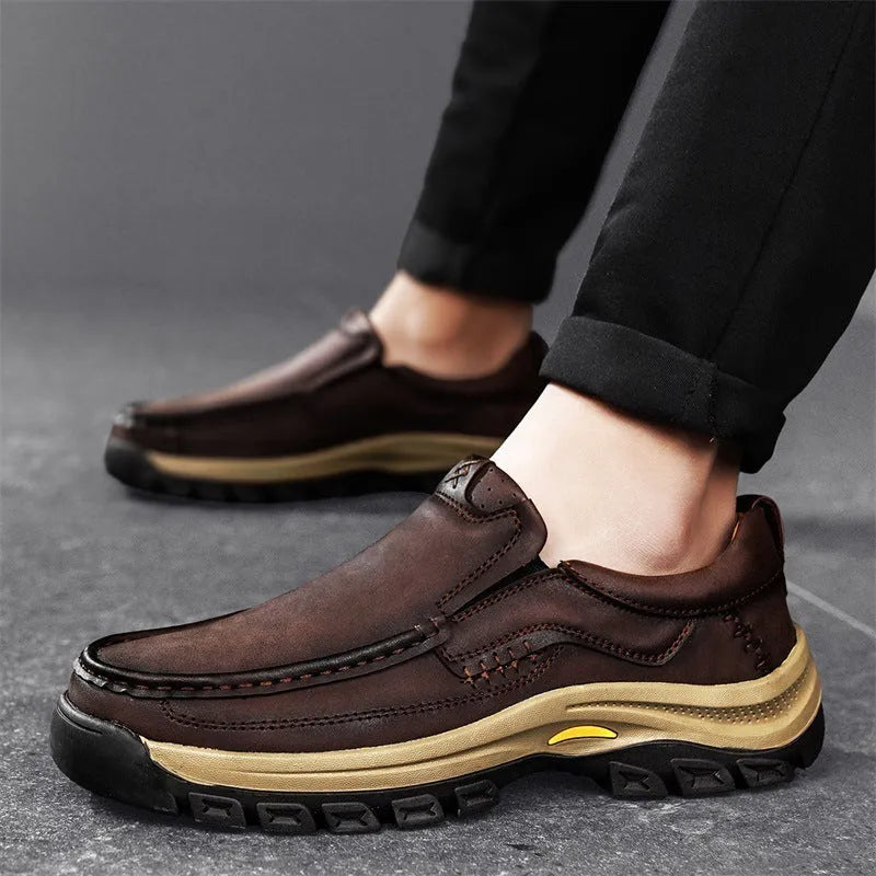 Men's black leather mountaineering shoes with thick rubber soles and round toe on a rocky path.