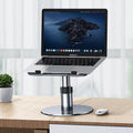 Silver adjustable laptop stand with 360-degree rotating base on a wooden desk.