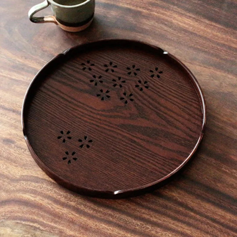 Twelve wooden dessert plates with carved cherry blossom design arranged in storage tray