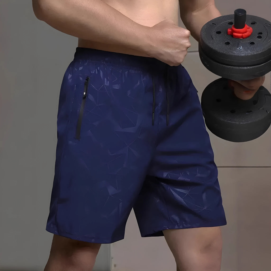 Man wearing loose fit black printed polyester sports shorts with elastic waistband on a beach.