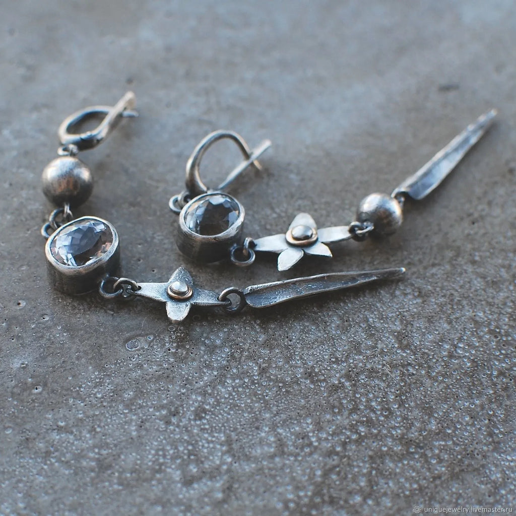Pair of long geometric pendant earrings in antique silver with rhinestone detail on a white background.