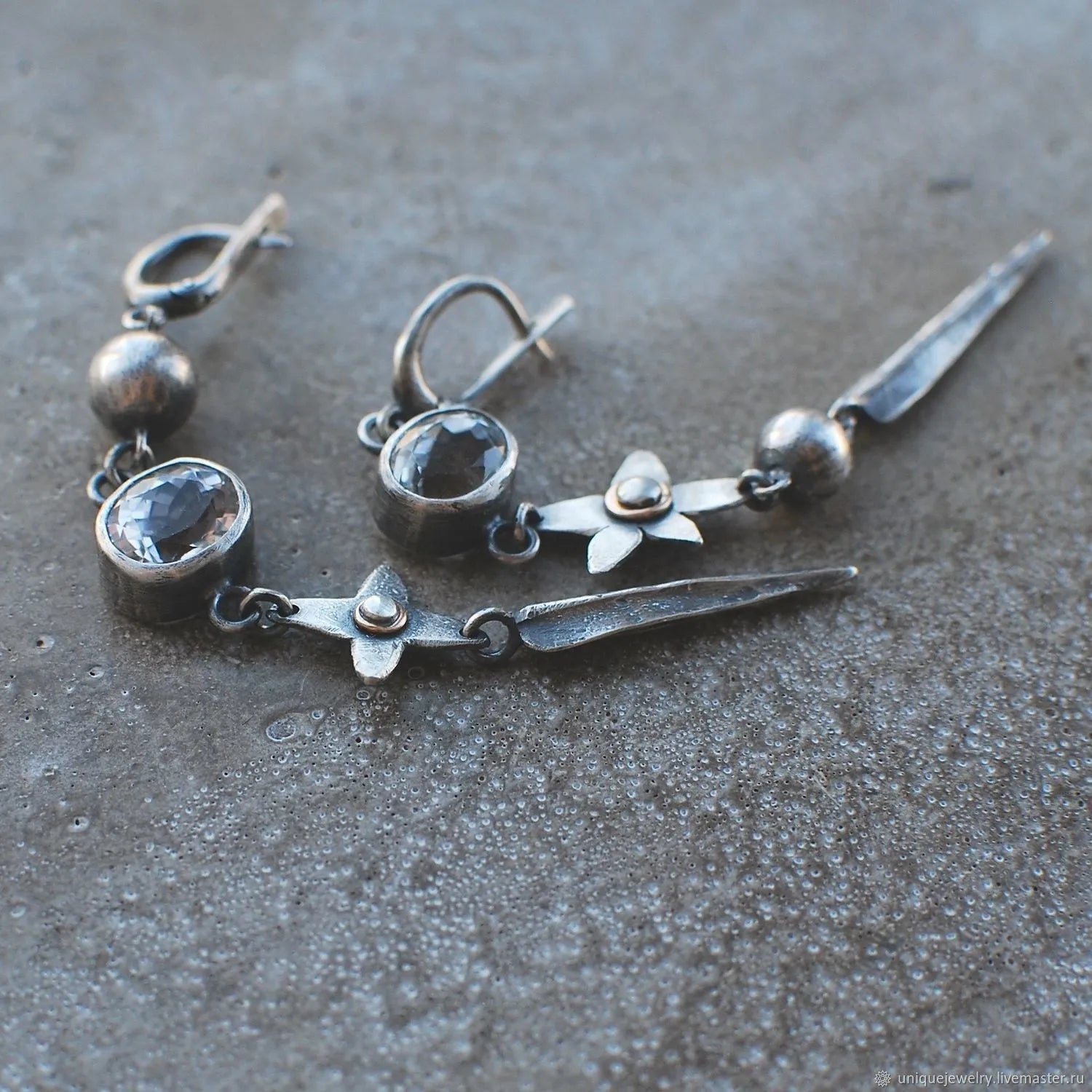 Pair of long geometric pendant earrings in antique silver with rhinestone detail on a white background.