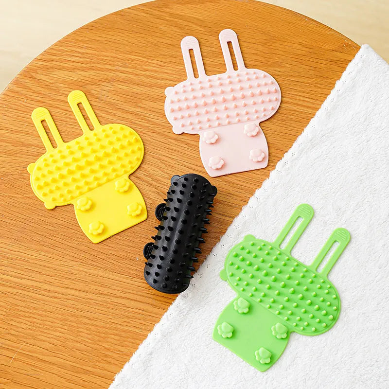 Silicone cat grooming comb with adjustable strap attached to furniture leg for scratching and hair removal