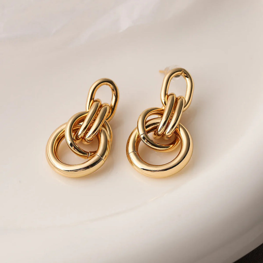 A pair of gold-colour geometric earrings with an irregular, high-profile design on a white background.
