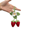 Handwoven strawberry-shaped car pendant made from cotton and hemp fibres on a grey background.
