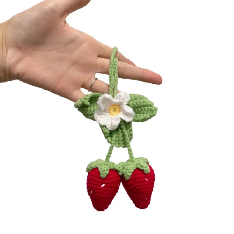 Handwoven strawberry-shaped car pendant made from cotton and hemp fibres on a grey background.