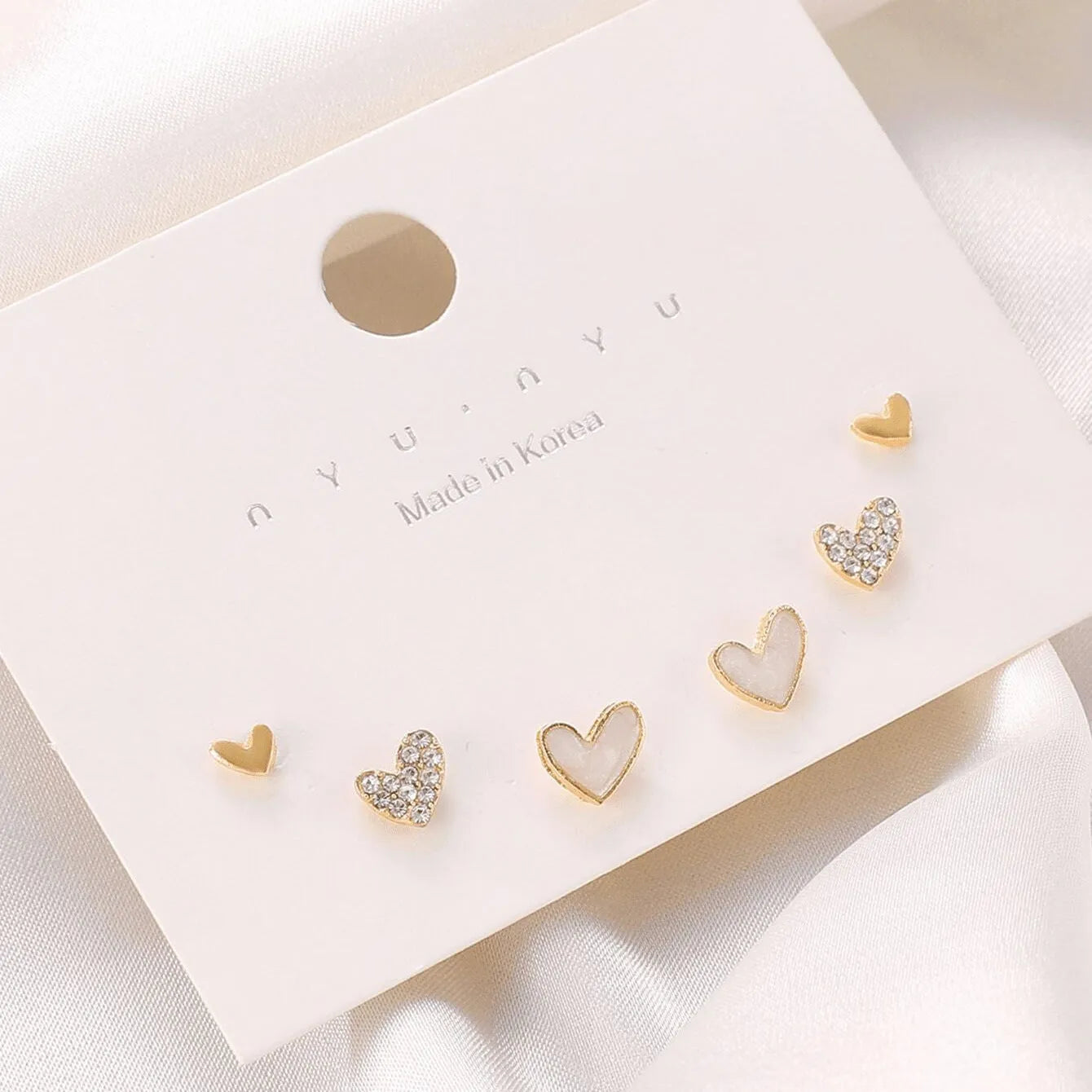 Three pairs of heart-shaped alloy earrings in gold, black, black and white, and pink colours on a white background.