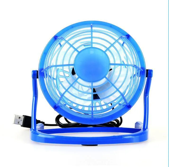 Small black USB desk fan with adjustable angle on wooden desk next to laptop
