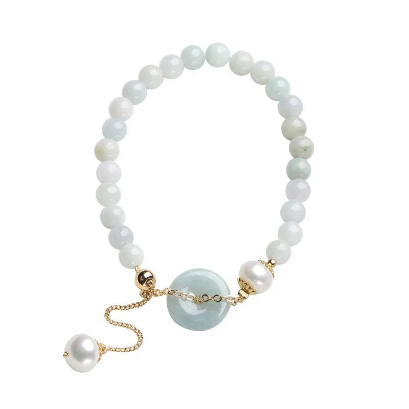 Close-up of a women's pearl bracelet with a natural emerald peace buckle charm and a jade round pendant.
