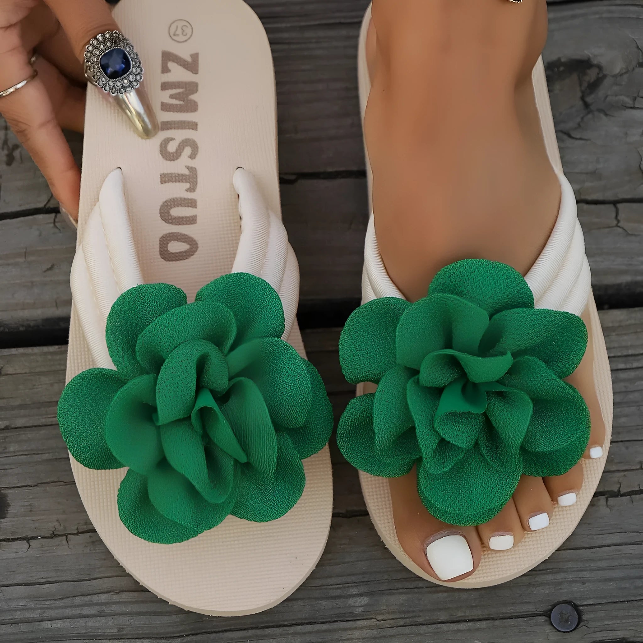 Plus size solid colour flip flop slippers with a flower detail on the upper, shown in beige.