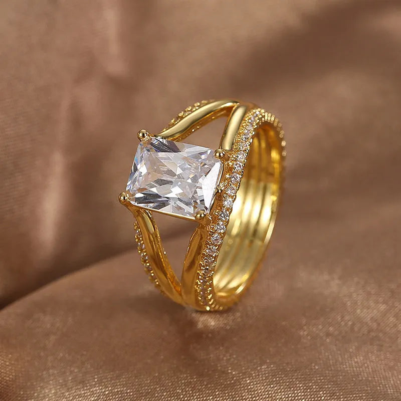 Gold-coloured geometric women's ring with a square zircon stone, shown on a finger.