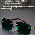 Frameless sunglasses with dark green lenses displayed alongside a protective hard case and cleaning cloth.