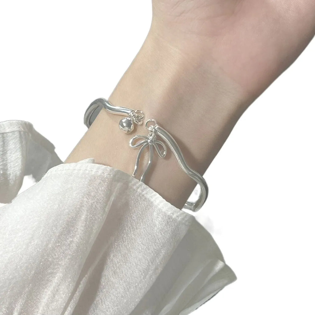Silver adjustable bracelet with a detailed bow charm and bell opening.