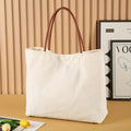 Beige white canvas tote bag with cotton handles, showing interior patch pocket and exterior zipper pocket.